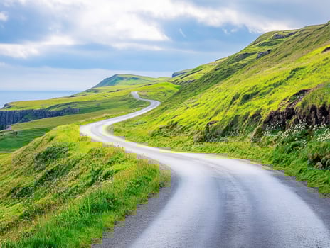Winding road through green hills by the coast under cloudy sky photo