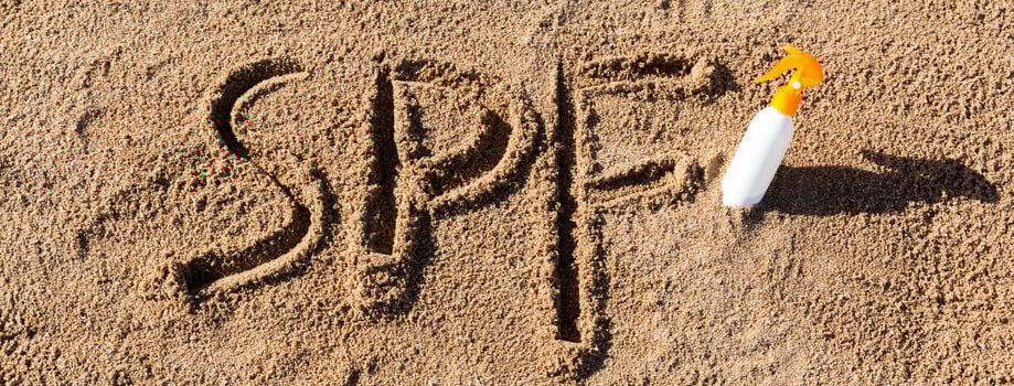 Sun protect factor. SPF word written the sand and white bottle with suntan cream. Skin care concept background photo