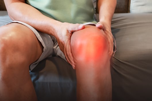 An elderly man sits on a sofa at home, holding his knee which is sore from osteoarthritis. Knee joint injury. photo