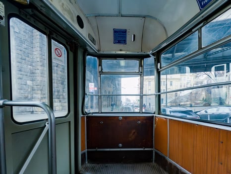 A nostalgic interior view of an old tram with worn wooden panels and metal railings, offering a glimpse of the city through large glass windows. photo