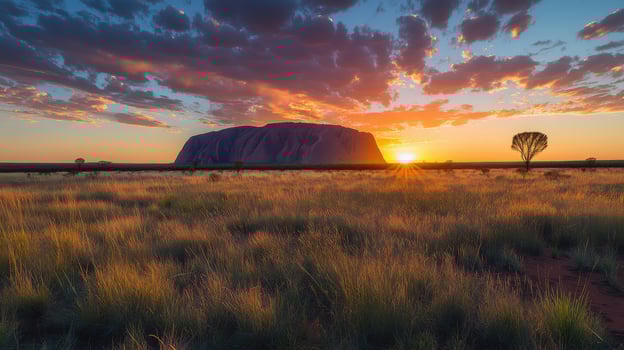 Desert rock formation at sunset. Field of grass in front of large stone. Orange sky with clouds above land. Remote nature scene. photo