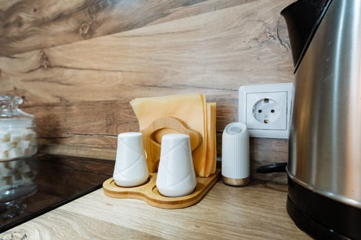 On the kitchen counter, there is a stylish electric kettle placed alongside salt and pepper shakers as well as a neatly arranged napkin holder, all essential items for cooking and dining photo