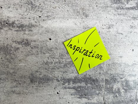 Bright yellow sticky note shaped as a diamond featuring the word Inspiration and decorative elements on a textured grey background, symbolizing the power of motivating ideas and creativity photo