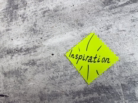 Vibrant yellow sticky note in a diamond shape displaying the word Inspiration with decorative elements on textured grey surface, representing the essence of motivating ideas and creative potential photo