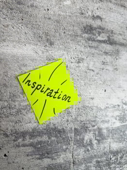 Bright yellow sticky note in a diamond shape featuring the word Inspiration and decorative rays on a textured grey background, symbolizing the spark of creativity and motivating ideas photo