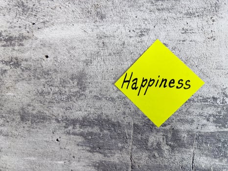 Bright yellow diamond-shaped sticky note with the word Happiness on a textured grey background, symbolizing joy and the importance of a positive outlook in daily life photo