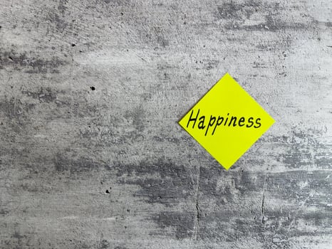 Bright yellow diamond-shaped sticky note with the word Happiness displayed on a textured grey background, representing joy, positivity, and the pursuit of a fulfilling life photo