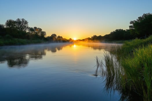 Golden sunrise paints misty river scene, light reflects on calm water surface photo