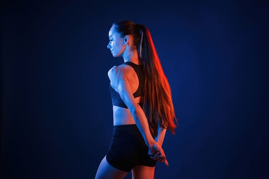 Rea,r view. Beautiful muscular woman is indoors in the studio with neon lighting photo