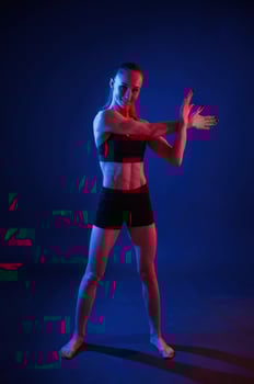 Preparing for sportive ,exercises. Warm up exercises. Beautiful muscular woman is indoors in the studio with neon lighting photo