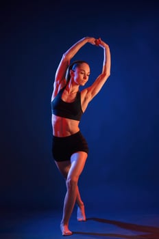 Sportive e,xercises, standing, and stretching the hands. Beautiful muscular woman is indoors in the studio with neon lighting photo