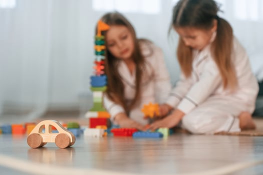 Close up view of little wooden car toy.. Two little girls are playing and having fun together in domestic room photo