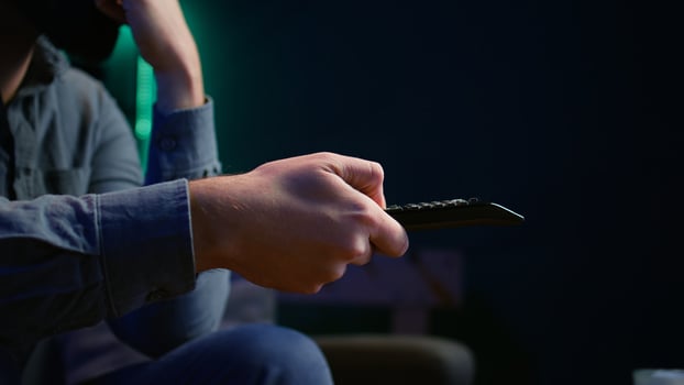 Close up of man on couch browsing through movies available on streaming service. Focus on remote control used by homeowner in apartment switching channels on TV, camera B photo