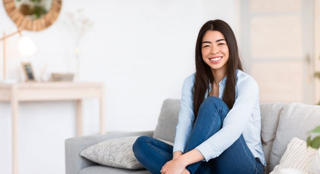 Cozy Weekend. Happy Young Asian Woman Sitting On Comfortable Sofa At Home, Posing And Looking At Camera, Sincerelly Smiling, Relaxing In Stylish Living Room, Enjoying Day Off, Copy Space photo