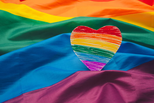 A rainbow heart shape symbol made from paper over the rainbow flag or LGBT flag background. photo
