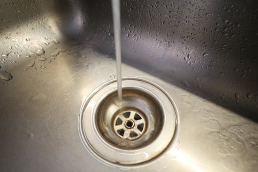 Water flowing into a stainless steel sink drain during a routine wash photo