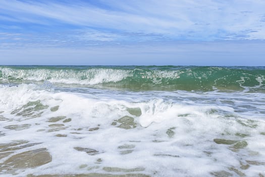 Blue cloudy sky above blue sea water, waves crashing sandy beach, windy weather. Summer vacation and holiday travel concept. Seascape nature background, beautiful sea shore with water foam photo