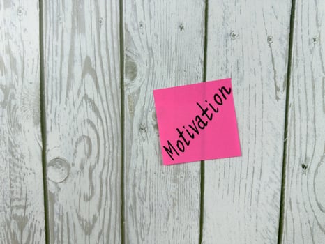 Pink sticky note with Motivation written on it, placed on a white wooden board. This image symbolizes motivation and commitment, ideal for conveying themes of drive and determination photo