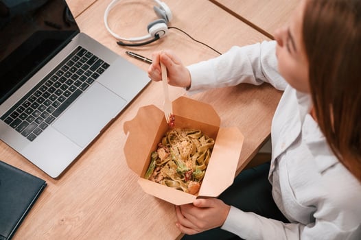 Businesswoman, in formal clothes is in the office eating udon that is in the eco box photo