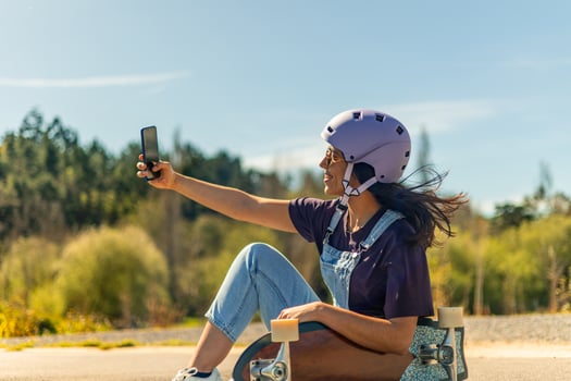 Latin skater taking a selfie with smartphone while sitting on her surfskate in pump track photo