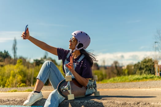 Young latin skater taking a selfie and making victory sign while sitting on her surfskate photo