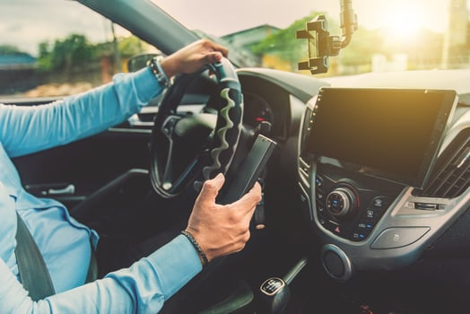 Driver hand on the steering wheel while using a cell phone. Man using phone while driving. Concept of irresponsible driving photo