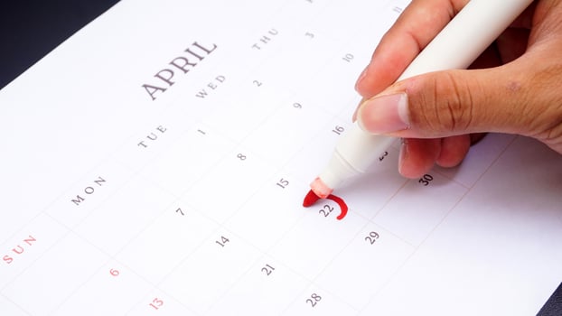 Hand holding marker to make mark on calendar at 22 of April as symbol of important day isolated on black background photo