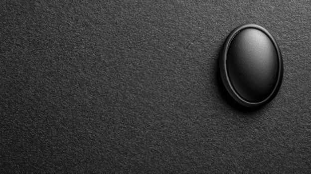 Black Oval Button on a Textured Dark Gray Surface in Monochrome photo
