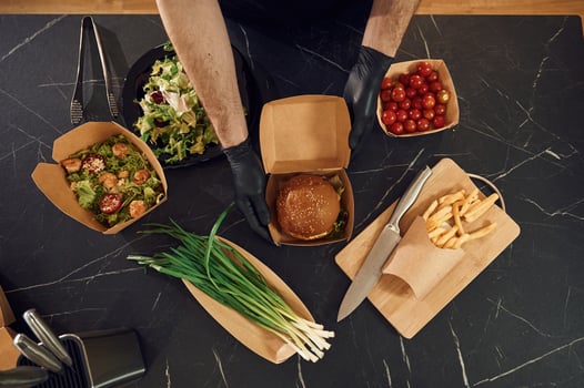 French, fries, vegetables and burger. Man is packing food into the paper eco boxes. Indoors, restaurant photo