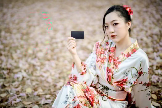 Beautiful Asian woman in traditional floral kimono holding black card while sitting on autumn leaf ground, Japanese style fashion concept photo