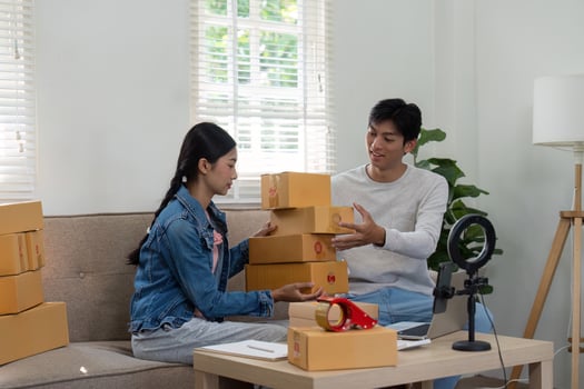 Product Preparation and Collaboration. An energetic couple organizes packages, preparing for a live online selling session. photo