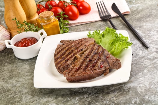 A plate of steak with a side of vegetables and a bottle of ketchup photo