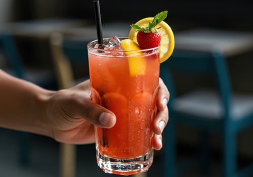A refreshing strawberry lemonade cocktail garnished with fresh fruit held in a hand. photo