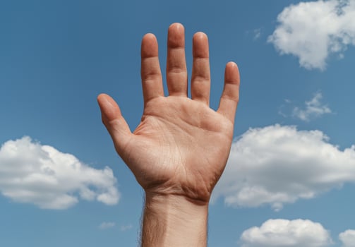 Hand raised against a blue sky with clouds photo