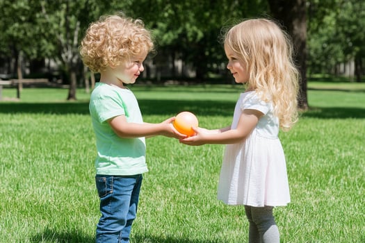 Two children holding an orange in a park photo
