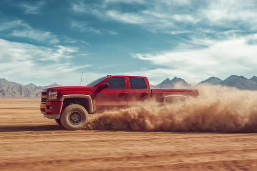 Red pickup truck driving on desert road leaving dust trail photo