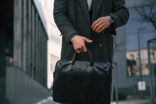 Man in ,black formal wear is standing outdoors and holding bag photo