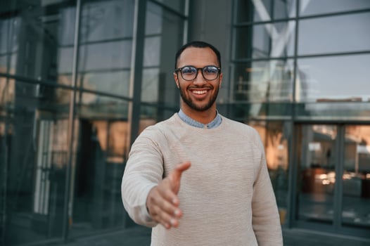 Giving greeting hand. Handsome black man is outdoors near the business building photo