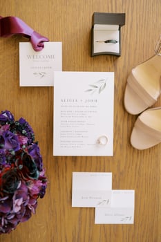 Engagement ring lies on the invitation next to the bouquet, the bride shoes and the groom tie photo