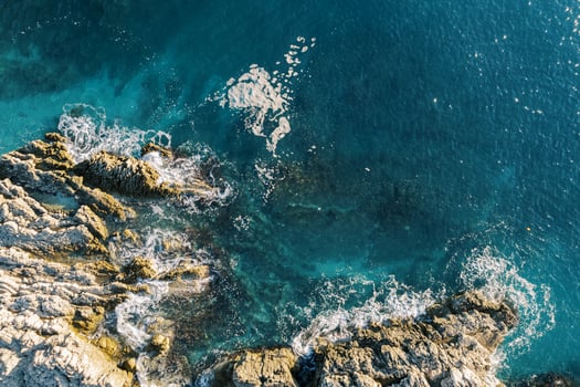 Surf hits the rocky, rugged shore. Top view photo