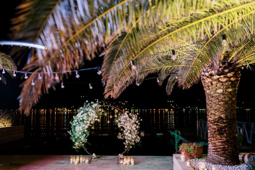 Lighted candles near a round wedding arch on the pier near a large palm tree photo