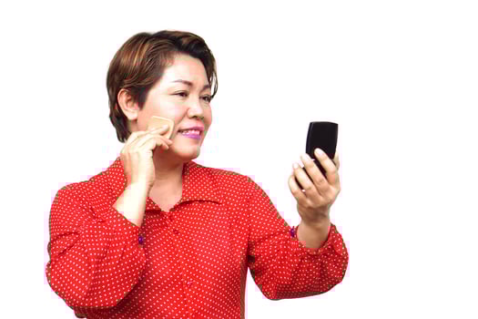 Asian middle aged woman is making up, using puff to apply powder on her face, looking at portable mirror Concept, women don't stop beauty, using cosmetics. Woman lifestyle, make self looks good photo