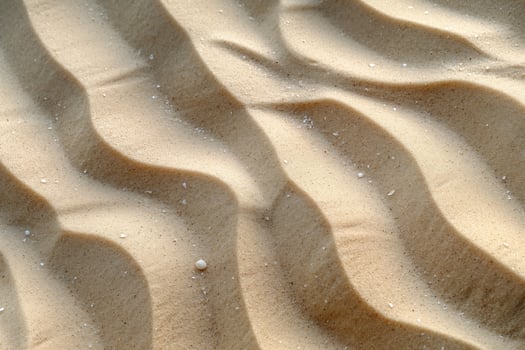 Close-up of smooth, undulating sand patterns illuminated by soft sunlight, creating a tranquil and serene atmosphere. photo