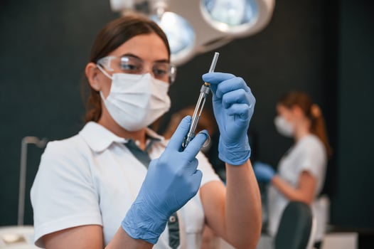 Doctor in ,blue glowes, is standing and holding equipment. In the stomatological cabinet photo