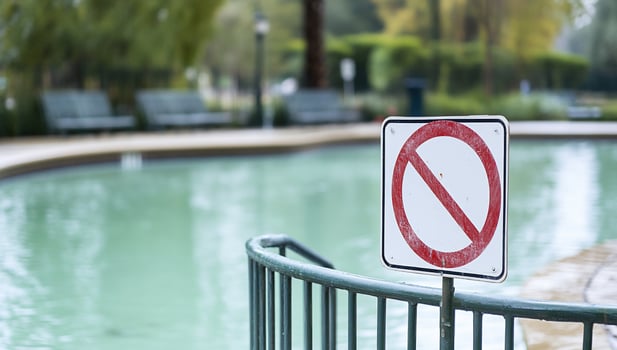 A no swimming sign near a green pool in a park setting. photo