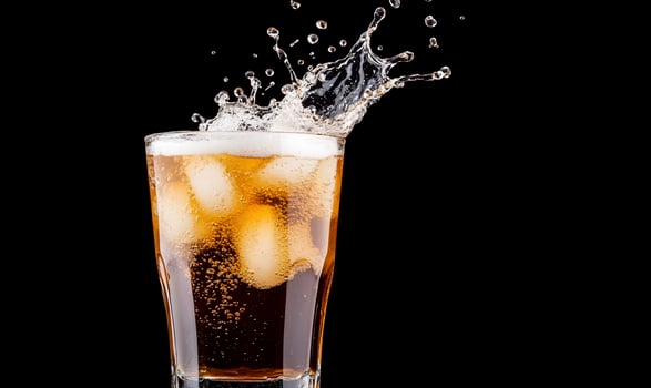A glass of carbonated beverage with ice, splashing against a dark background. photo