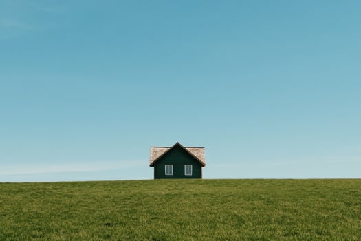 Small, green house on a grassy hill against a clear blue sky photo