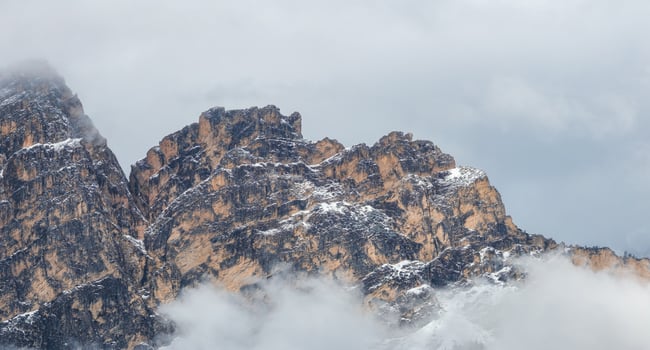 Rugged mountain peaks in the Dolomites, Italy, partially covered in mist and snow. Light and shadow highlight the jagged texture of the rocky formations. photo