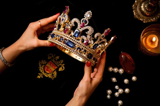 Holding a regal crown adorned with pearls and gemstones beside candlelight on a dark surface showcasing intricate royal symbolism photo