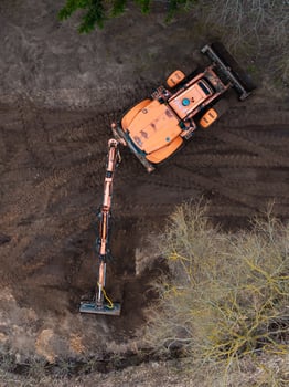 Aerial View of Orange Excavator on Dirt Surface with Sparse Vegetation photo